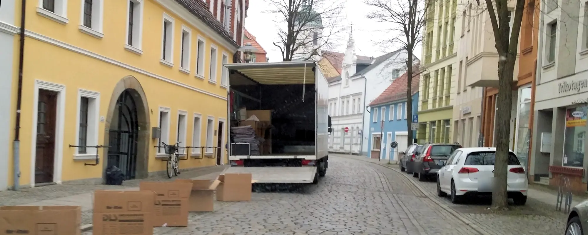 Umzugs-LKW mit DLS-Kartons in einer engen Gasse mit Kopfsteinpflaster