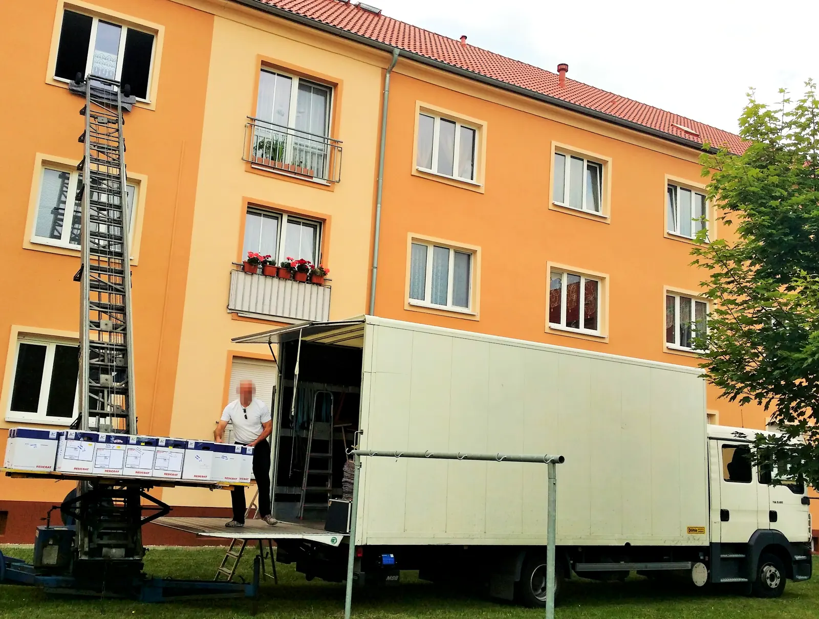 DLS-Umzugs-LKW mit ausgefahrenem Möbellift vor einem Wohnhaus